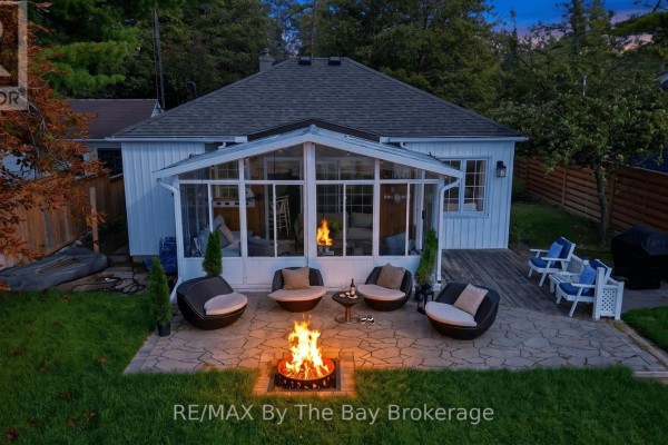 Rear exterior of the cottage showcasing a sunroom, patio with fire pit and outdoor seating. - 150 Santos Lane, Wasaga Beach