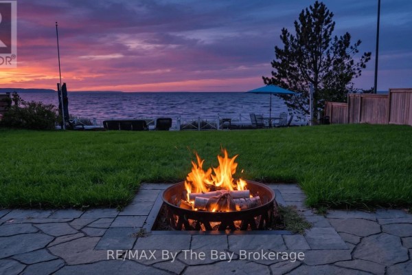 Outdoor fire pit on a stone patio overlooking the water during a colorful sunset. - 150 Santos Lane, Wasaga Beach