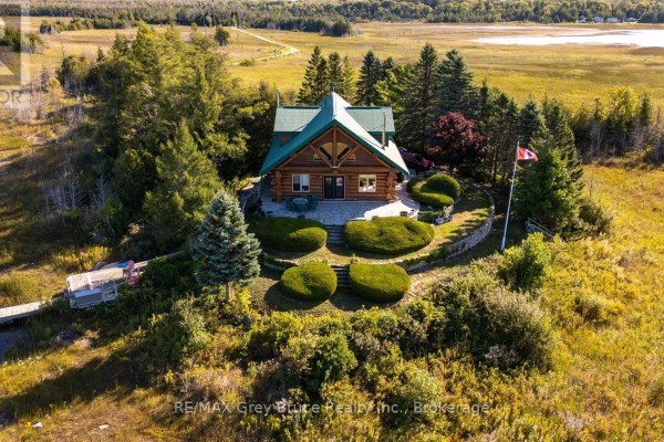 Front view of a log cabin with a stone walkway leading to the entrance and manicured shrubs on the lawn. - 150 Shoreline Avenue, South Bruce Peninsula