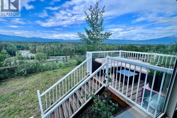 Deck with white railings, glass panels, and outdoor furniture overlooks a scenic valley and tree line. - 1500 2nd St. (aldermere Ridge), Telkwa
