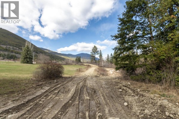 View from a wooded area overlooking a valley with distant mountains, fields, and a body of water. - 1500 60 Street Sw, Salmon Arm