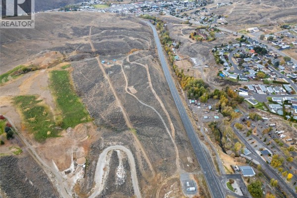 Aerial view of a long, paved road running through a semi-arid landscape with scattered trees and residential properties on the right. - 1500 Fehr Way, Cache Creek