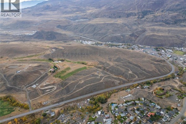 Distant aerial view of mountainous terrain surrounding a valley with a town, showcasing undeveloped land along a highway. - 1500 Fehr Way, Cache Creek