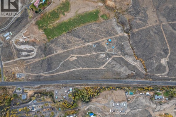Top-down aerial view of rough, undeveloped land with a paved road in the foreground and scattered structures and trees. - 1500 Fehr Way, Cache Creek