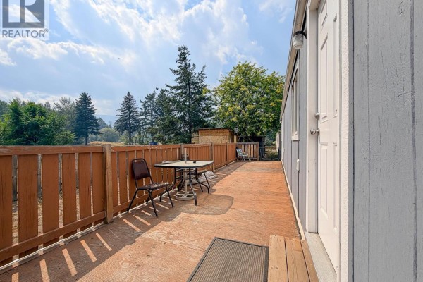 Wooden deck of a mobile home with chairs, table, and a view of trees. - 1500 Spring Street Unit# 6b, Merritt