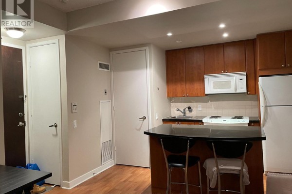 Kitchenette with dark wood cabinets, white appliances, and a black breakfast bar with stools. - 1501 - 85 Bloor Street E, Toronto