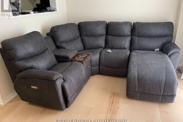 Corner view of a large, dark grey reclining sectional sofa on a light wood floor. - 1501 Rankin Way, Innisfil