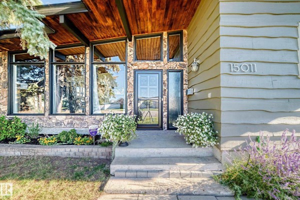 Front entrance with stone and wood details, large windows, and blooming white flowers. - 15011 55 St Nw, Edmonton