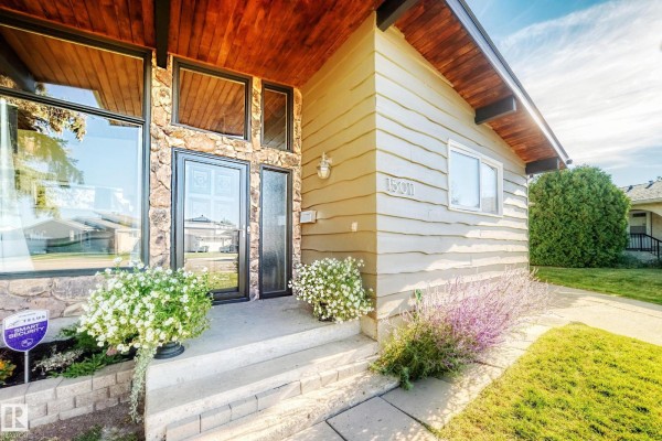 Close-up of the entrance showing stone and wood siding, with potted plants. - 15011 55 St Nw, Edmonton