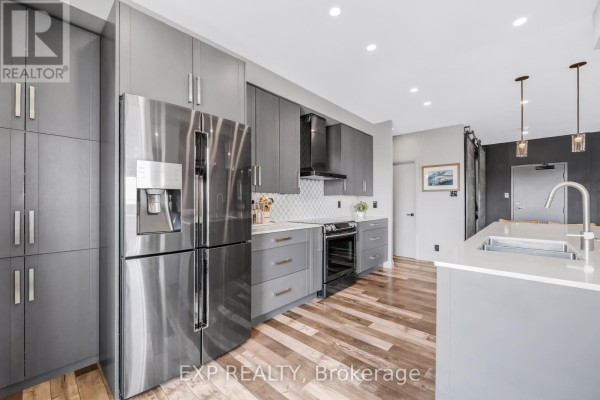 Kitchen features grey cabinetry, a stainless steel refrigerator, and a gas range with a black hood fan. - 1502 - 65 Ellen Street, Barrie