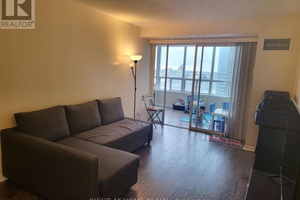 Living room with grey sectional sofa and large window. - 1502 - 88 Corporate Drive, Toronto