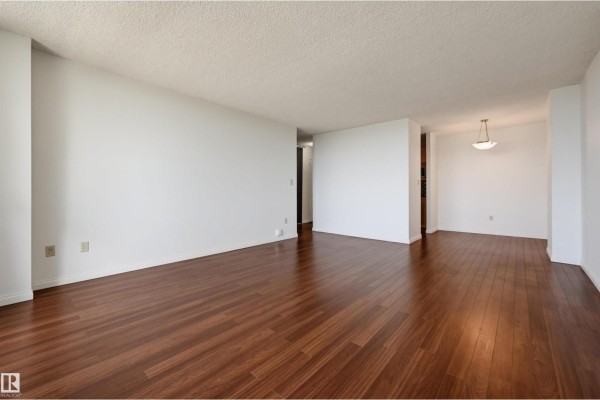 Empty living and dining area with dark wood floors and white walls. - #1502 13910 Stony Plain Rd Nw, Edmonton