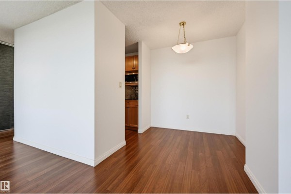 Dining area with dark wood floors, white walls, and a view into the kitchen. - #1502 13910 Stony Plain Rd Nw, Edmonton