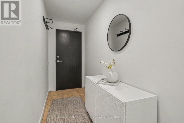 Apartment entryway with a dark wood door, white cabinet, round mirror, and textured rug. - 1503 - 33 Charles Street E, Toronto