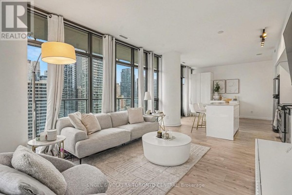 Living room featuring a grey sectional sofa, a round coffee table, and large windows with city views. - 1503 - 33 Charles Street E, Toronto