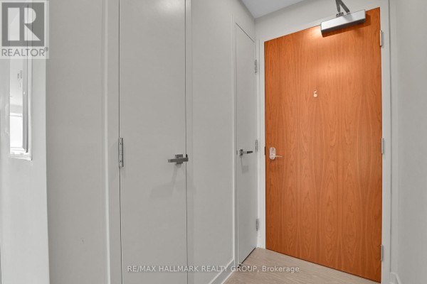 Apartment hallway with a light wood door, white closet doors, and brushed metal hardware. - 1504 - 101 Queen Street, Ottawa