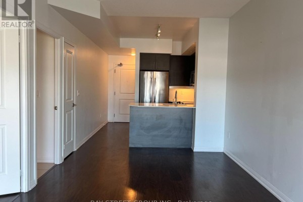 Interior view of apartment hallway and open concept kitchen with stainless steel appliances and dark wood flooring. - 1504 - 65 East Liberty Street, Toronto