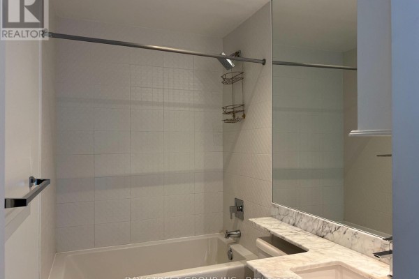 Bathroom with white tiled walls, bathtub, shower, and a large mirror over the vanity. - 1504 - 65 East Liberty Street, Toronto