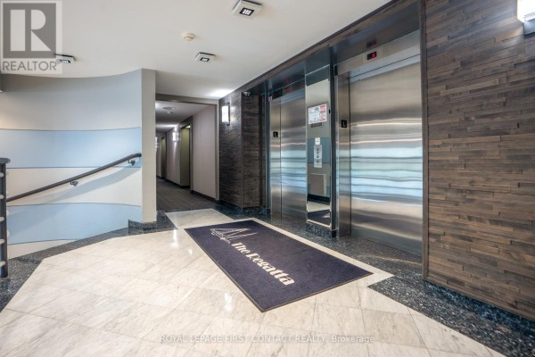 Apartment building hallway with elevators, tiled floor, and welcome mat. - 1504 - 75 Ellen Street, Barrie