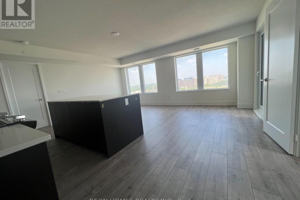 Bright living area with light wood floors, a large dark kitchen island, and multiple windows overlooking the city. - 1506 - 10 Eva Road, Toronto