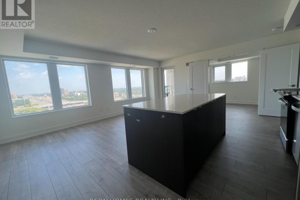 Spacious living area with a large kitchen island, light wood floors, and wide windows showing a city view. - 1506 - 10 Eva Road, Toronto