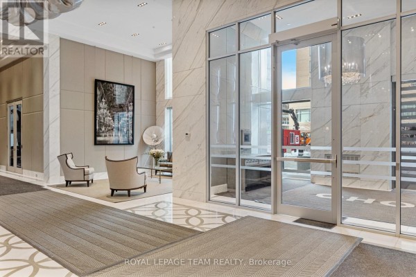 Building lobby entrance with marble walls, glass doors, two chairs, and artwork on the wall. - 1506 - 111 Champagne Avenue S, Ottawa