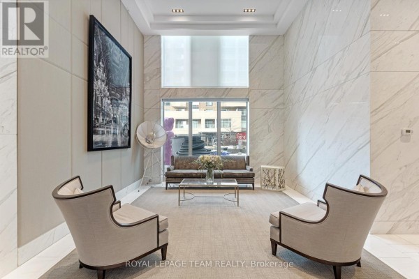 Lobby seating area with two chairs facing a sofa and coffee table, set against a marble wall. - 1506 - 111 Champagne Avenue S, Ottawa