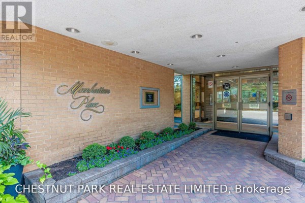 Entrance to Manhattan Place with a curved brick wall, planters, and glass doors under a covered walkway. - 1506 - 131 Beecroft Road, Toronto