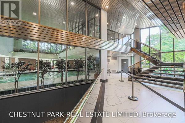 Indoor swimming pool viewed through a glass partition from a lobby with a marble floor and metal staircase. - 1506 - 131 Beecroft Road, Toronto