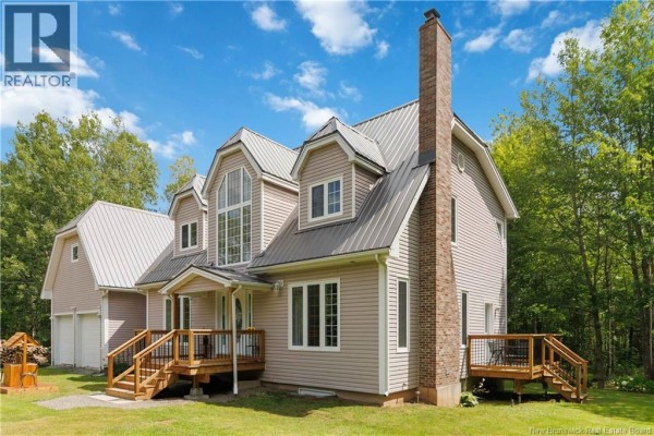Side view of the house showing a brick chimney, wooden deck, and attached garage. - 1507 Shediac River Road, Shediac River