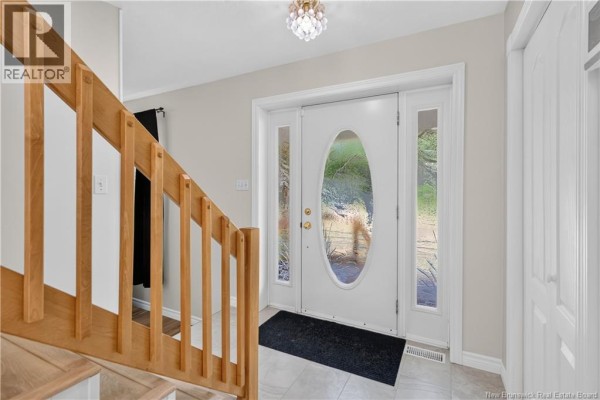 Interior view of a home entryway with a white door, sidelights, and wooden staircase. - 1507 Shediac River Road, Shediac River