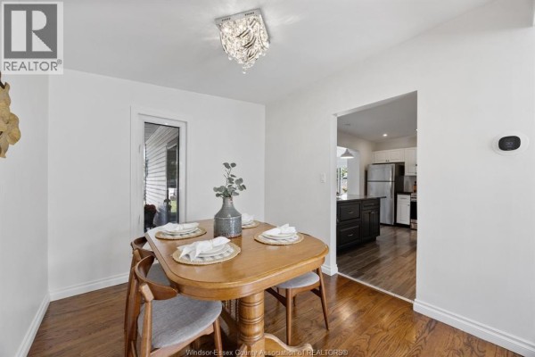 Dining room with a wooden table set for four, chairs, and view into the kitchen with dark cabinets. - 1507 St. Gabriel, Windsor
