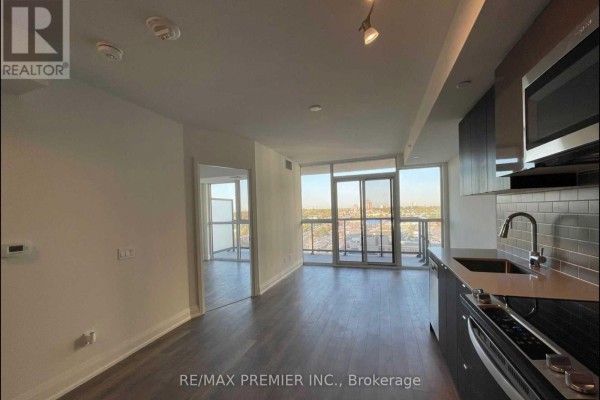 Living area with a view of the city skyline through glass doors and a glimpse into another room. - 1508 - 1461 Lawrence Avenue W, Toronto