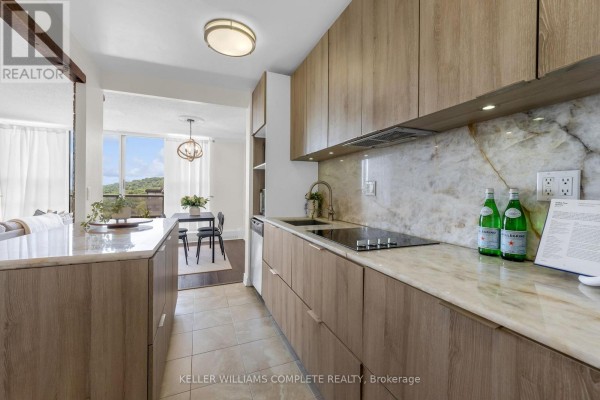 View of the galley kitchen with wood cabinetry and marble countertops, opening to dining area. - 1508 - 1964 Main Street W, Hamilton