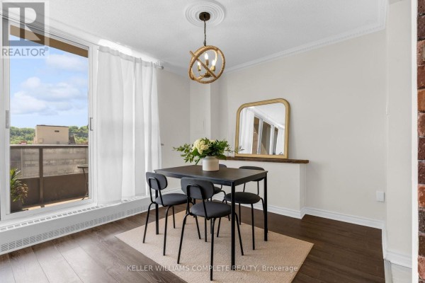 Dining area with a table, four chairs, rug, mirror on wall, and large window with white curtains. - 1508 - 1964 Main Street W, Hamilton