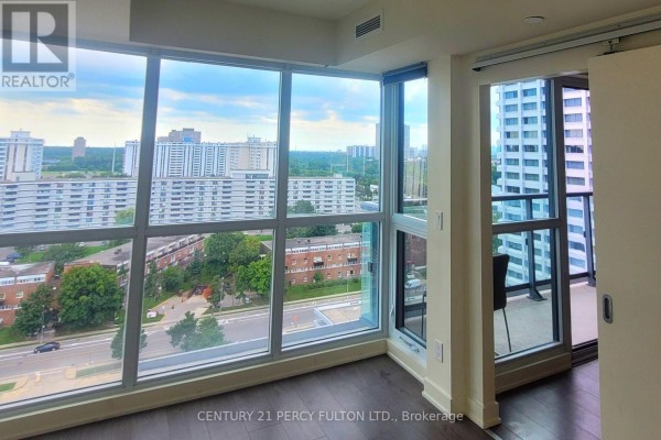 Interior view of an empty room with floor-to-ceiling windows and a balcony overlooking city buildings. - 1508 - 2 Sonic Way, Toronto