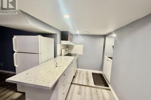 A view of a small kitchen with a white refrigerator, an island with granite countertop, and grey walls. - 1508 Major Oaks Road, Pickering
