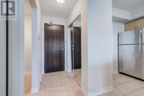Apartment entryway with a dark wood door, mirrored closet, and beige tile flooring. - 1509 - 15 North Park Road, Vaughan