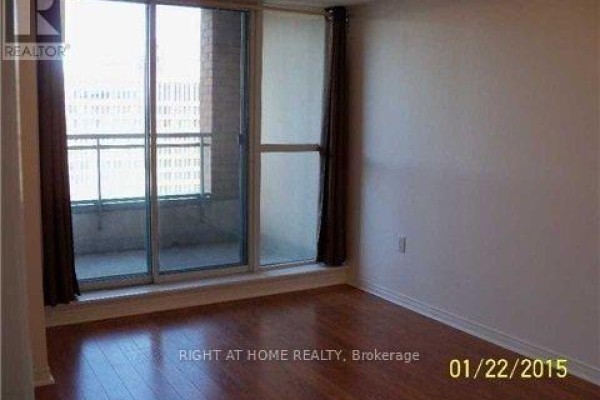 A bedroom with hardwood floors, large sliding glass doors, and dark brown curtains. - 1509 - 887 Bay Street, Toronto