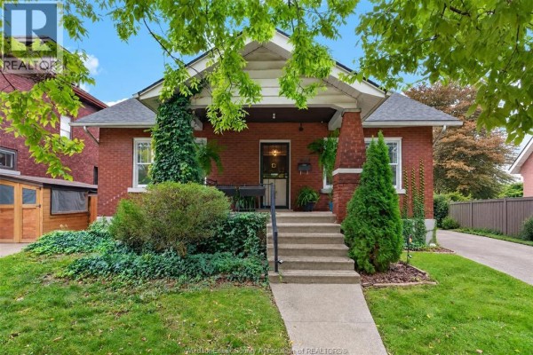 Front view of a red brick house with a covered porch, stone steps, and surrounding greenery. - 1509 Church, Windsor
