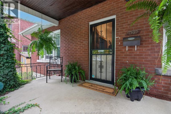 Front porch of a brick house with a metal screen door, chair, potted ferns, and welcome mat. - 1509 Church, Windsor