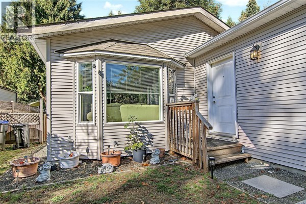 Close-up of the house exterior showing a bay window, wooden steps leading to a white front door, and siding. - 1509 Mason Trail, Parksville