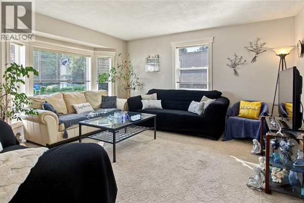 Living room with beige carpet, a large bay window, a cream sofa, and a black sofa with pillows. - 1509 Mason Trail, Parksville