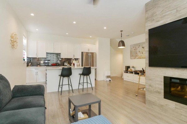 Open concept living area showing a white kitchen with island, stools, stainless steel appliances, and dining area. - 151 16433 19 Avenue, Surrey