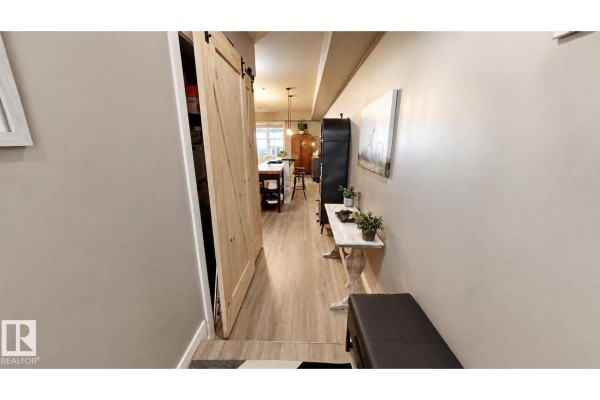 Hallway with a light wood barn door leading to a kitchen and living area. - #151 4827 104a St Nw Nw, Edmonton
