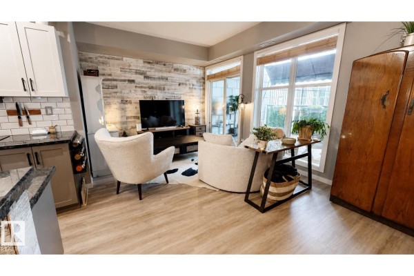 Living room with a TV, two accent chairs, and a wooden cabinet next to a window. - #151 4827 104a St Nw Nw, Edmonton