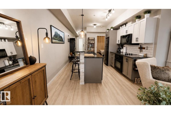 Open-concept living space showing a kitchen island, dining area, and living room with furniture. - #151 4827 104a St Nw Nw, Edmonton