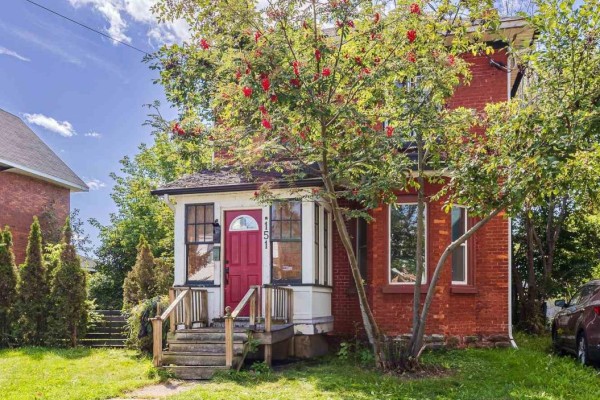 Front view of a red brick house with a covered porch and a row of manicured hedges. - 151 Albert St E, Sault Ste  Marie
