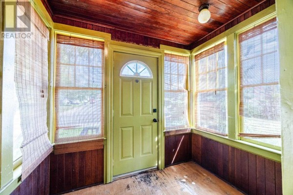 Interior view of a sunroom with bamboo blinds, wood paneling, and a green door. - 151 Albert St E, Sault Ste  Marie