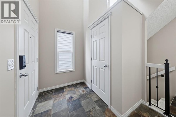 Entrance foyer with slate tile flooring, a window, and two white doors. - 151 Copperfield Common Se, Calgary